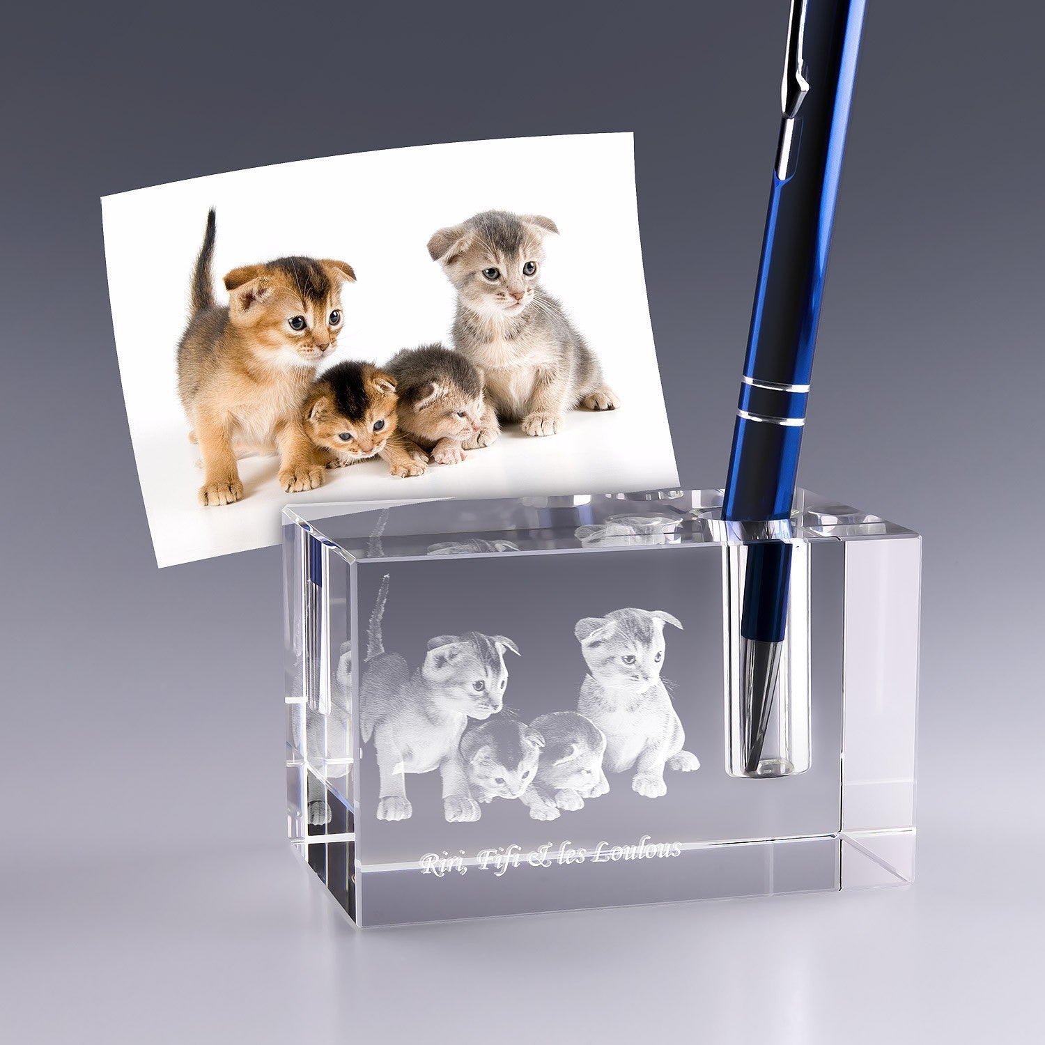 Bloc en verre gravé en 3D représentant des chatons, utilisé comme porte-stylo personnalisé, avec un stylo bleu inséré dans l’emplacement prévu.