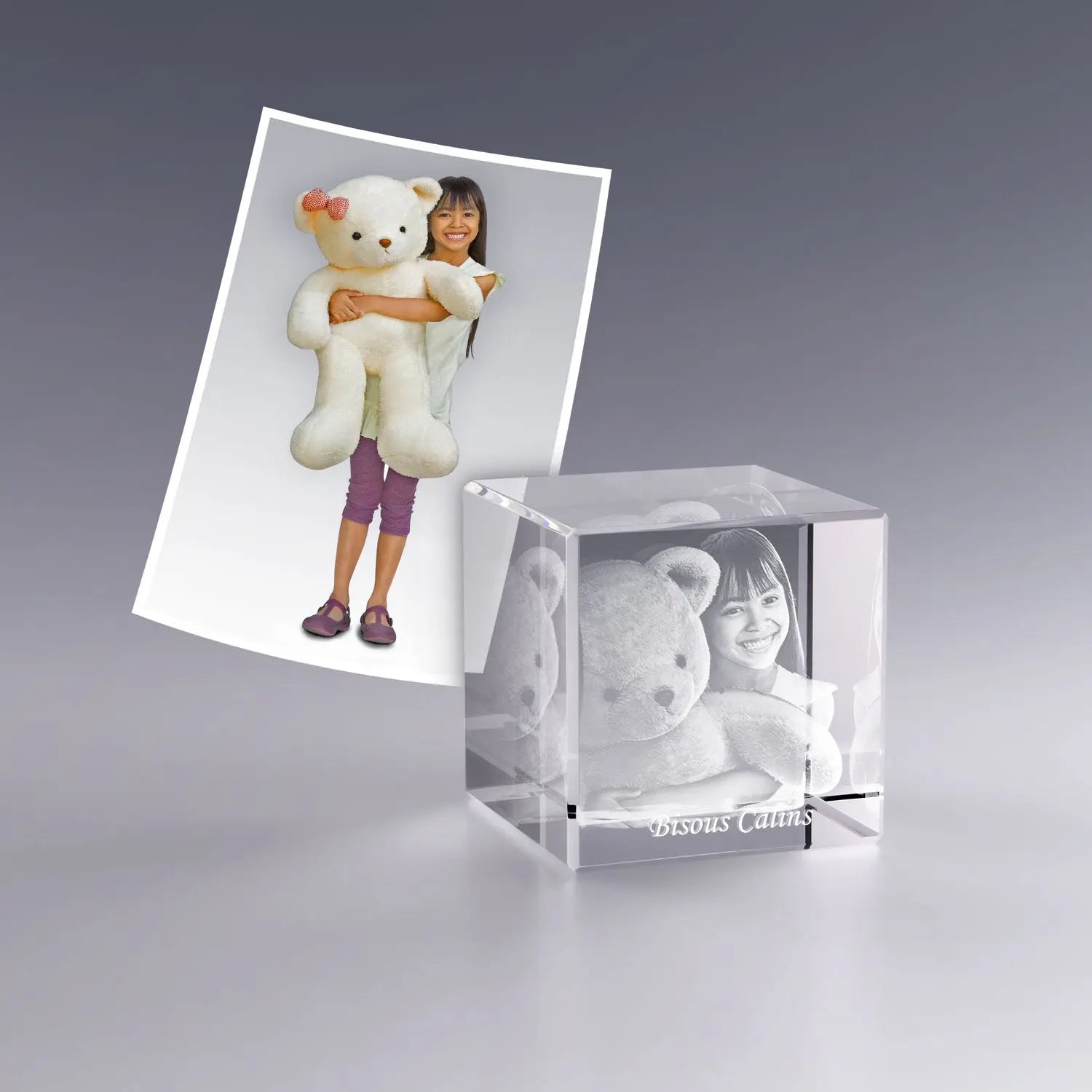 Gravure laser 3D dans un cube en verre de 4 cm représentant une enfant serrant un gros ours en peluche, avec l’inscription "Bisous Câlins".