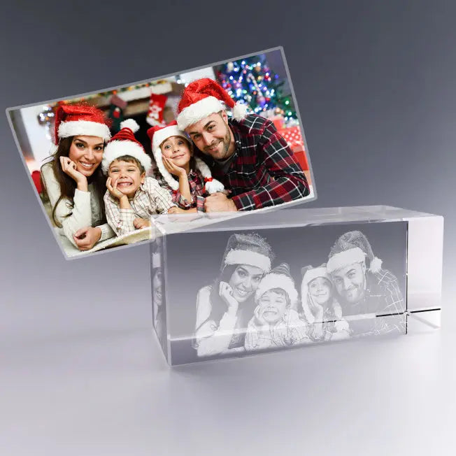 Bloc en verre rectangulaire gravé en 3D avec le portrait d’une famille portant des bonnets de Noël, reproduit à partir de la photo en couleur posée derrière.