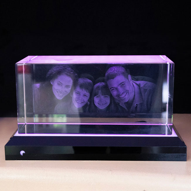 Bloc en verre rectangulaire gravé en 3D avec le portrait d’une famille, posé sur un socle lumineux à éclairage violet diffus.