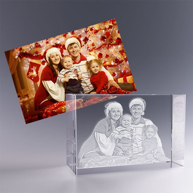 Bloc en verre gravé en 3D avec le portrait d'une famille en tenue de Noël, inspiré de la photo en couleur posée derrière, décor festif en arrière-plan.