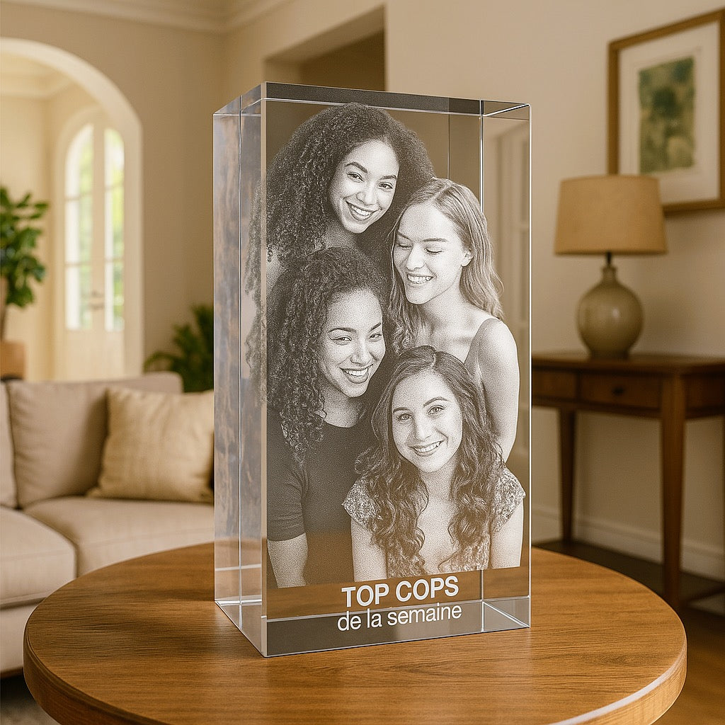 Bloc en verre vertical de 30 cm gravé en 3D avec cinq amies souriantes et l’inscription “TOP COP’S de la semaine”, posé sur une table dans un salon.