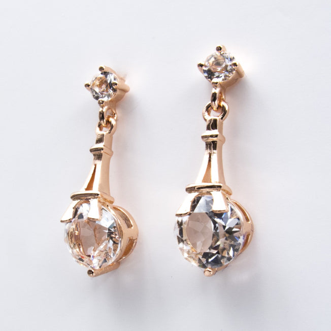 Boucles d’oreilles pendantes en or rose, avec cristaux Swarovski® sertis sous une Tour Eiffel stylisée. Bijou romantique et lumineux.