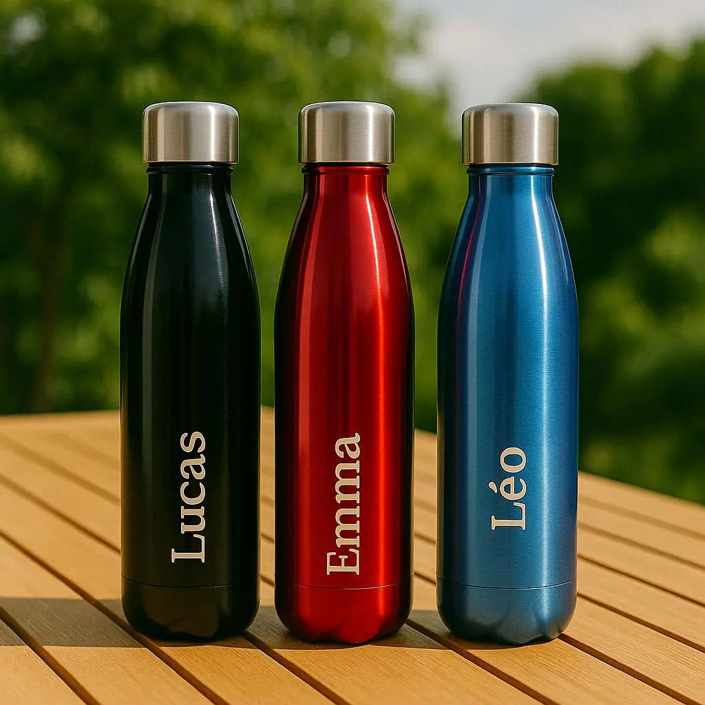 Trio de bouteilles isothermes personnalisées avec les prénoms Lucas, Emma et Léo, posées sur une table en bois à l’extérieur.