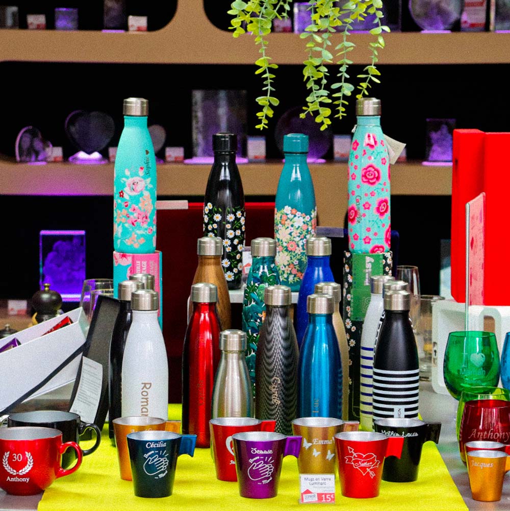 Bouteilles isothermes et mugs personnalisés exposés dans la boutique Zephyr Paris, avec gravures de prénoms et motifs variés sur fond d’étagères lumineuses.