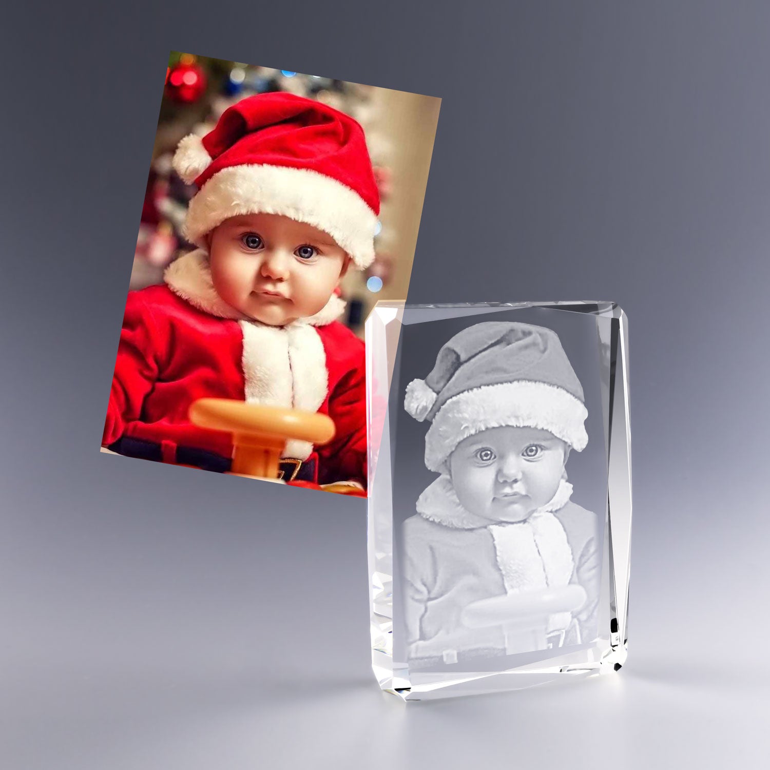 Gravure 2D d’un bébé en tenue de Noël dans un bloc vertical facetté en verre, avec un bonnet rouge et un regard attendrissant.