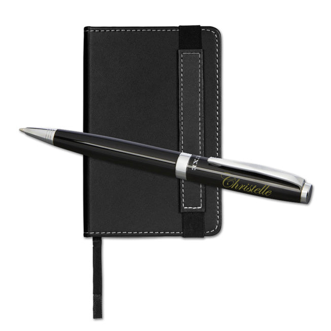 Stylo personnalisé noir posé sur un petit carnet noir avec surpiqûres blanches, formant un ensemble élégant et pratique à offrir en cadeau.