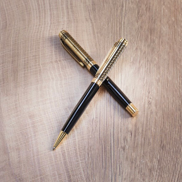 Parure Legato dorée personnalisable composée d’un stylo bille et d’un stylo roller noir et or posés en croix sur une table en bois — cadeau d’affaires élégant et raffiné.