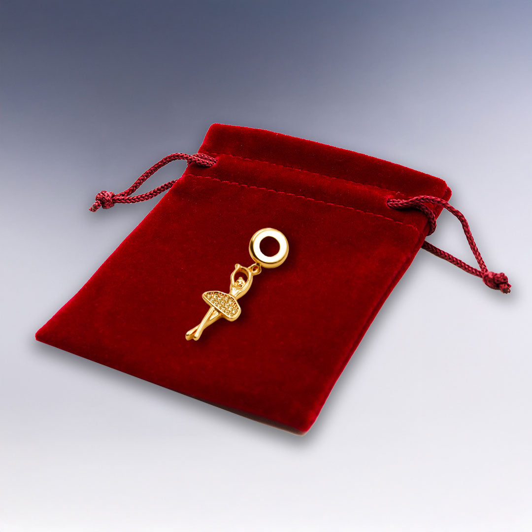 Charm Ballerine doré rose élégant, présenté sur une pochette suédine rouge. Un bijou raffiné pour bracelet, parfait pour les passionnées de danse classique.
