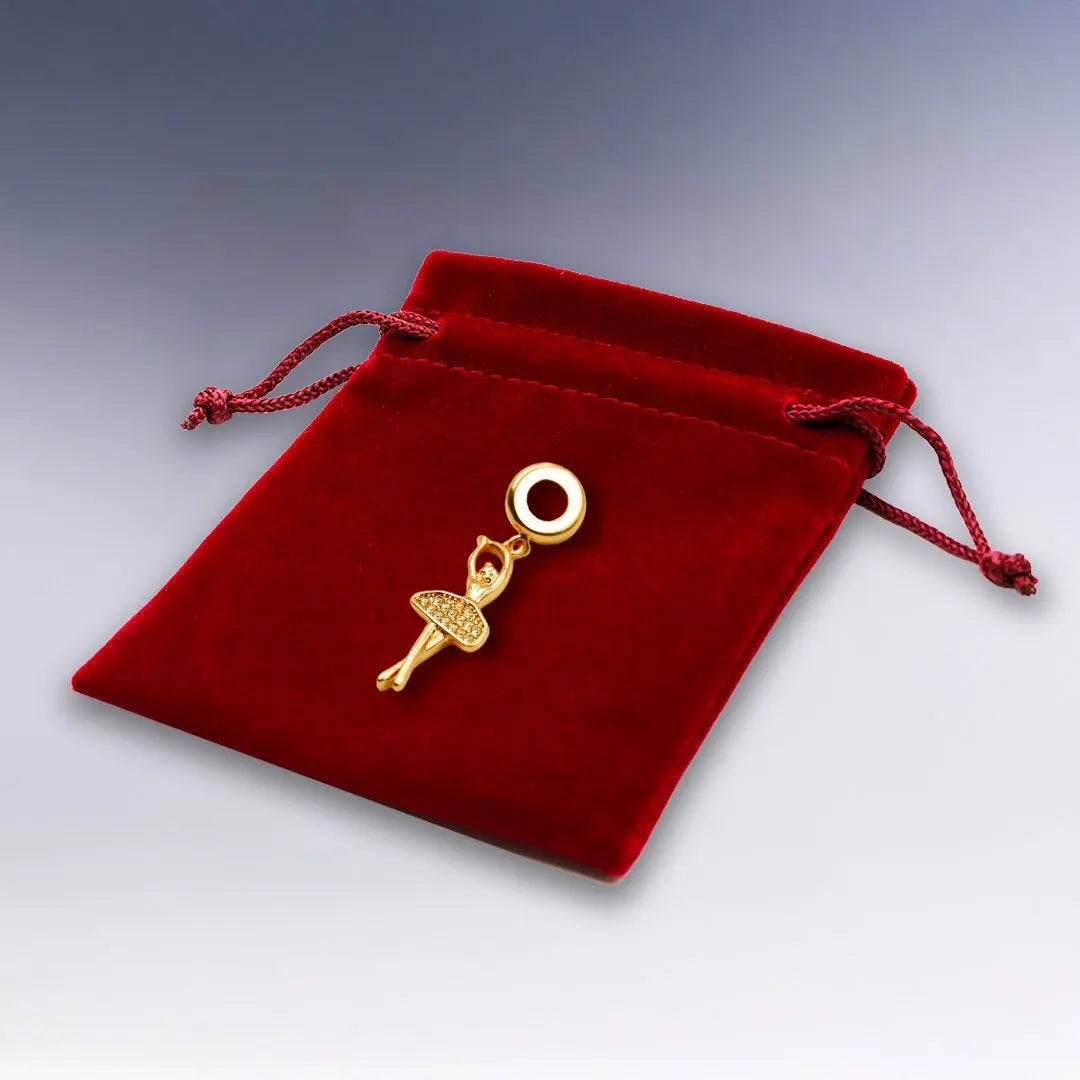 Charm Ballerine doré rose élégant, présenté sur une pochette suédine rouge. Un bijou raffiné pour bracelet, parfait pour les passionnées de danse classique.