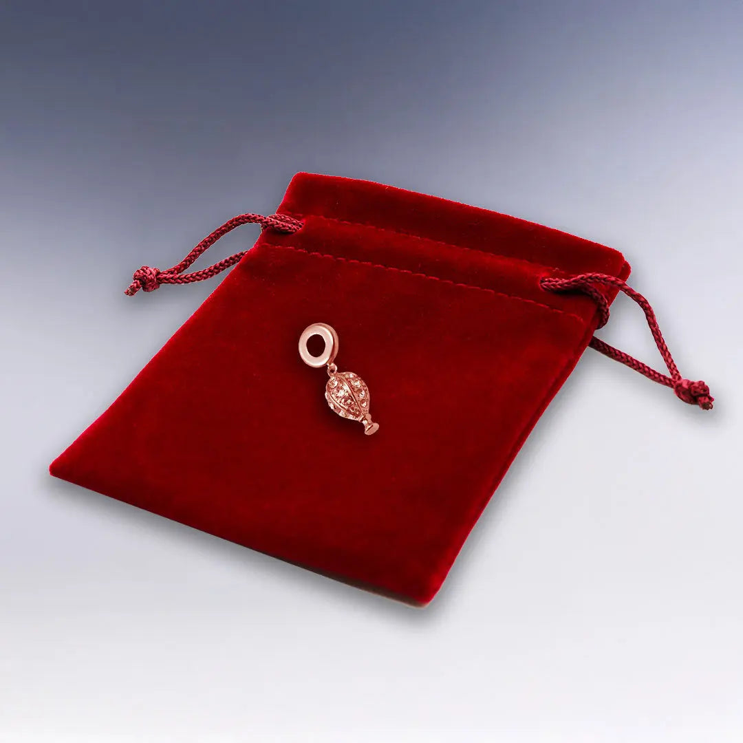 Charm ballon en doré rose brillant, présenté sur une élégante pochette en suédine rouge pour bracelet raffiné et original.