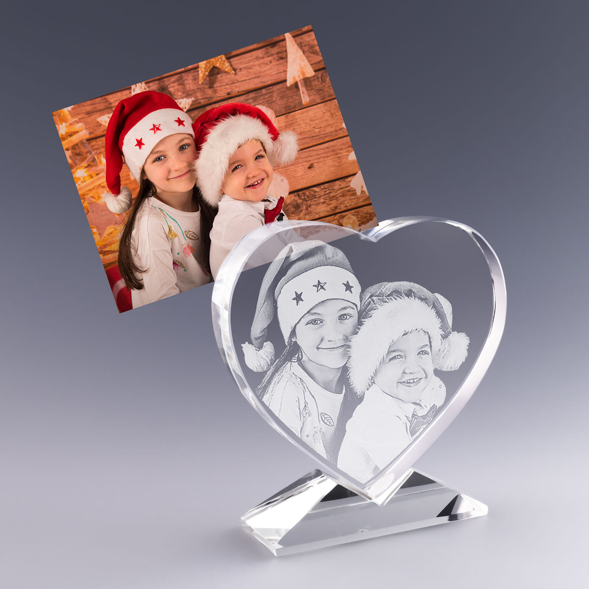 Cœur en Verre Gravé 2D avec photo et texte personnalisés – Cadeau de Noël – Deux enfants souriants portent des bonnets rouges devant un décor en bois festif. Leur image est gravée avec finesse dans un cœur en verre sur socle, un cadeau personnalisé plein de tendresse pour célébrer la magie de Noël.