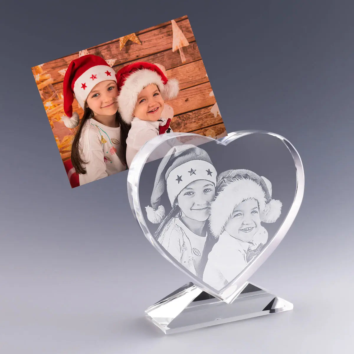 Cœur en Verre Gravé 2D avec photo et texte personnalisés – Cadeau de Noël – Deux enfants souriants portent des bonnets rouges devant un décor en bois festif. Leur image est gravée avec finesse dans un cœur en verre sur socle, un cadeau personnalisé plein de tendresse pour célébrer la magie de Noël.