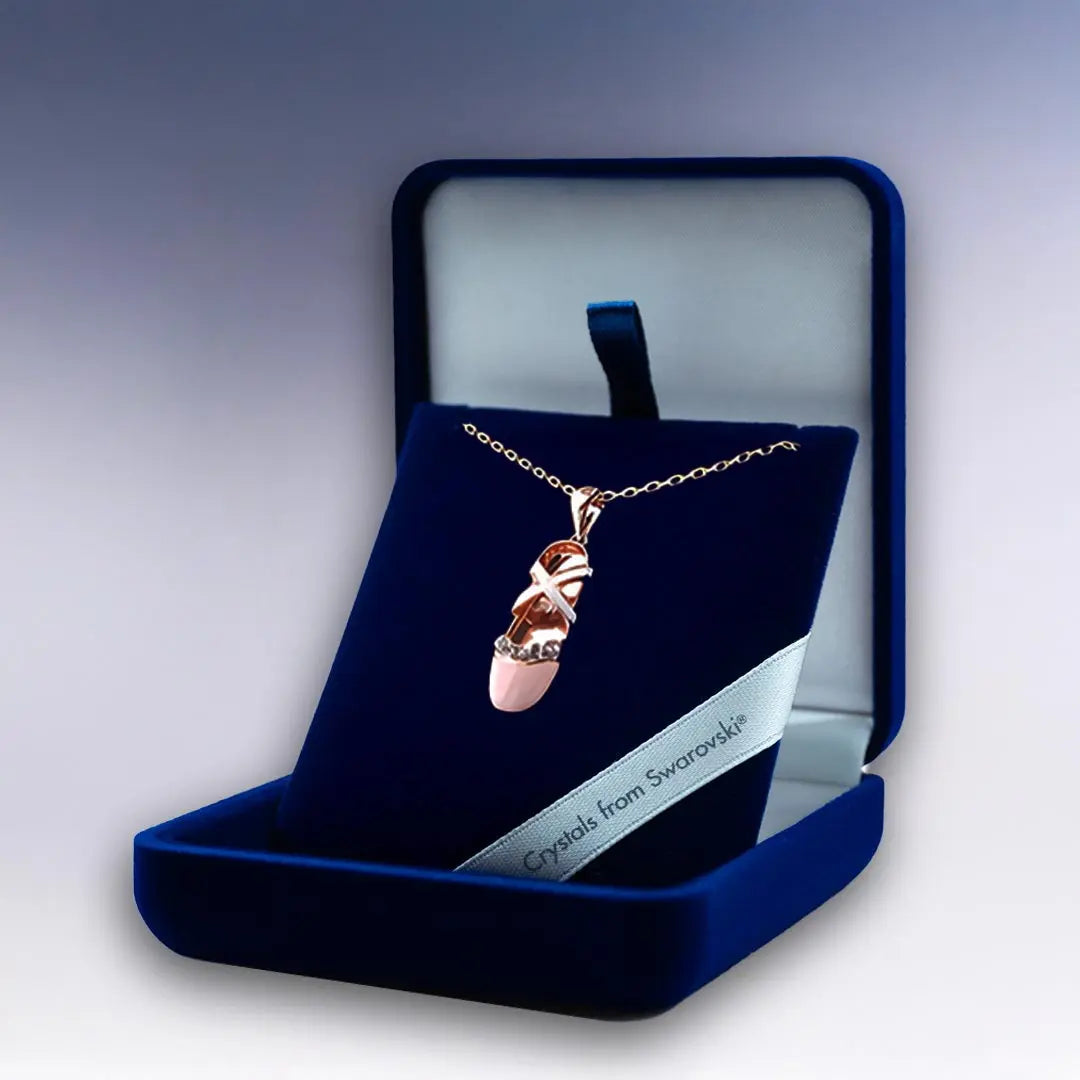 Collier pendentif en forme de chausson de ballerine plaqué or rose, orné de cristaux Swarovski®, présenté dans un élégant écrin bleu.