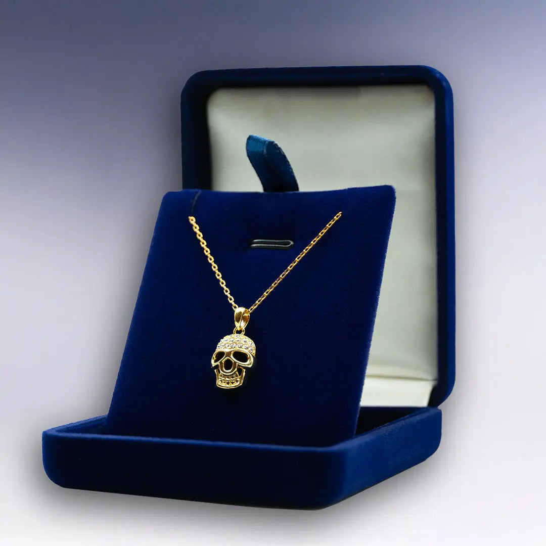 Collier Tête de Mort doré dans boîte bleu velours ouverte, design éclatant et esprit rebelle assumé.