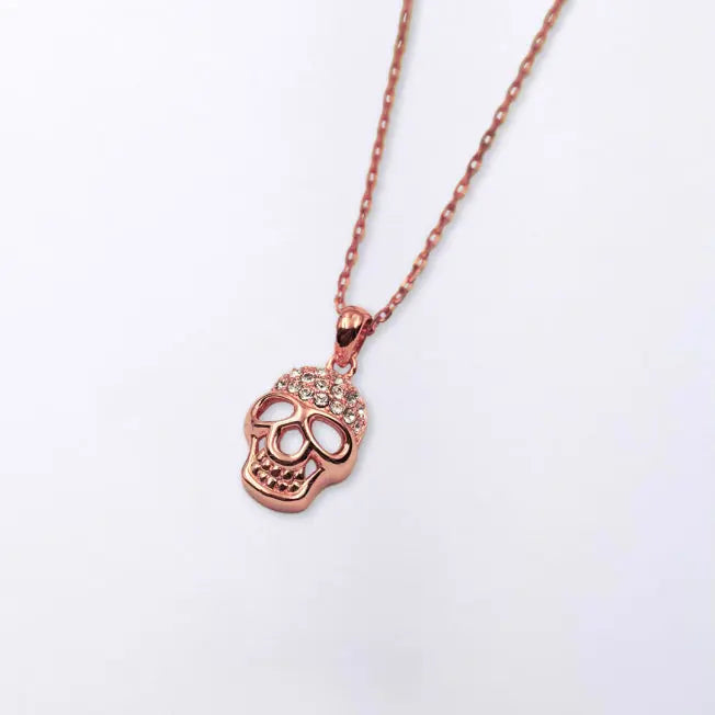 Collier Tête de Mort rose doré présenté sur fond blanc, chaîne fine et pendentif orné de strass.