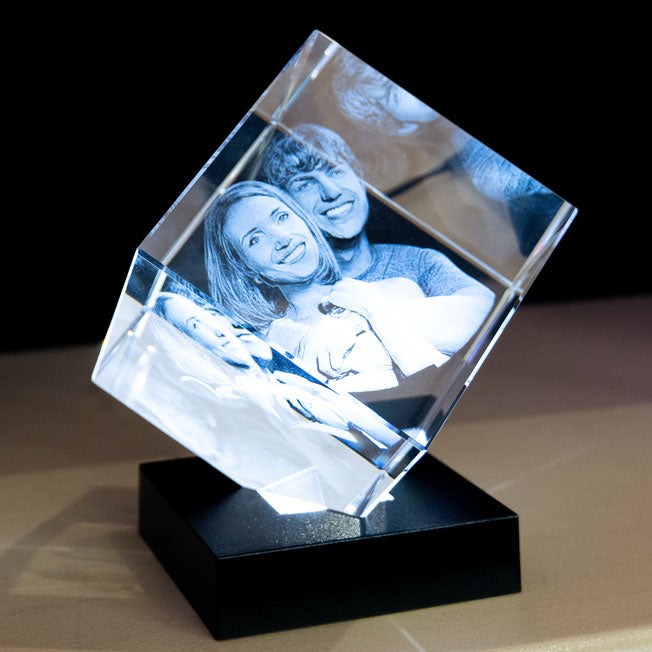 Cube en verre pan coupé gravé au laser, mettant en lumière une photo 3D d'une famille souriante sur socle lumineux.
