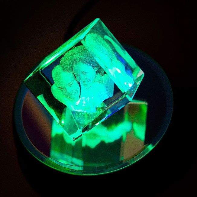 Cube en verre pan coupé de 5 cm gravé en 3D avec une photo de couple, posé sur un socle lumineux à LED bleue. Cadeau unique en verre.