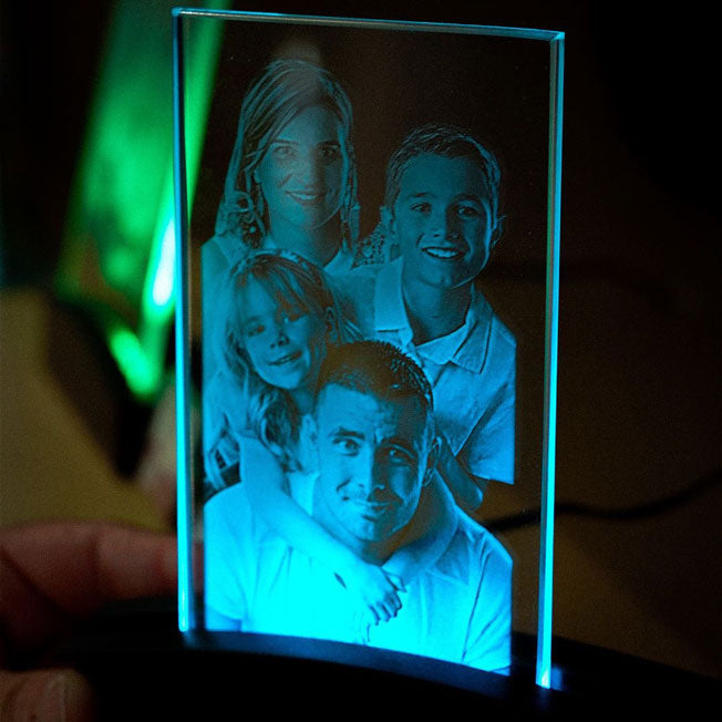 Cadeau unique : plaque en verre verticale avec gravure 2D d’une photo de famille, mise en valeur par une lumière LED bleu turquoise.