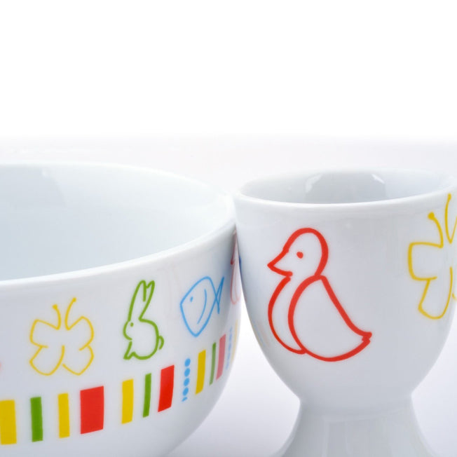 Zoom sur le bol et le coquetier décorés de motifs animaux colorés : lapin, poisson, canard, papillon. Une vaisselle ludique pour enfant.