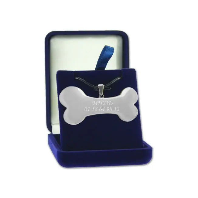 Pendentif en forme d’os argenté personnalisable avec nom et numéro de téléphone, présenté dans un écrin en velours bleu.