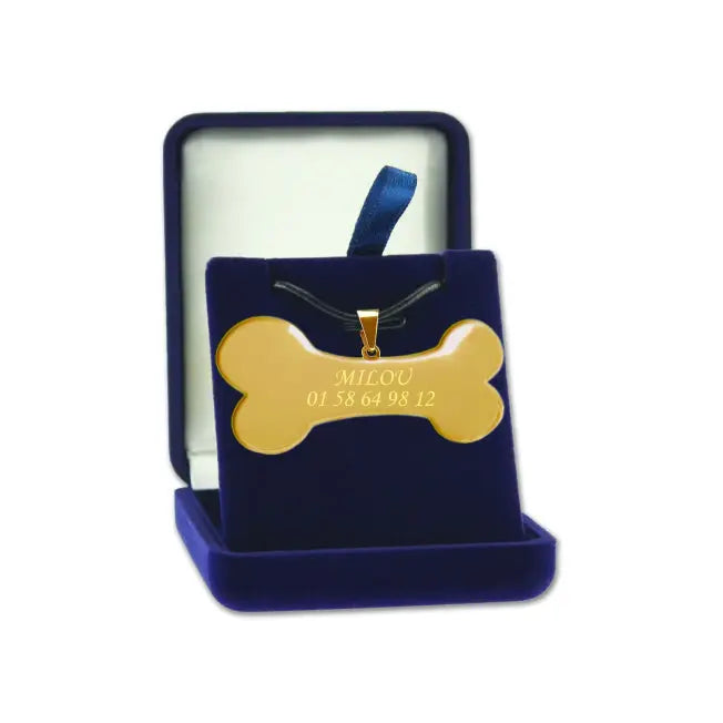 Pendentif en forme d’os doré personnalisable avec nom et numéro de téléphone, présenté dans un écrin en velours bleu.