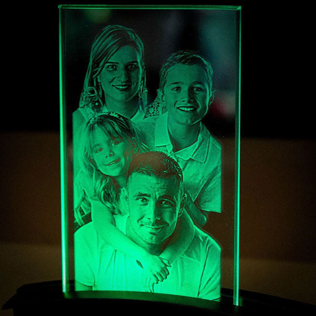 Portrait de famille gravé en 2D dans une plaque en verre vertical, éclairée par un socle lumineux vert, parfait comme cadeau personnalisé.