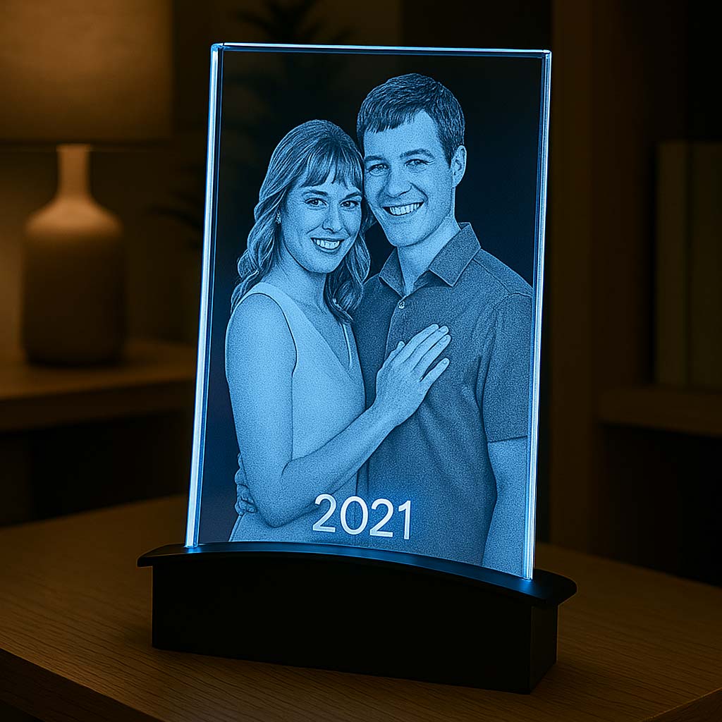 Plaque en verre rétroéclairée en bleu par un socle tunnel LED. Le couple souriant et l’année gravée ressortent parfaitement dans un décor chaleureux.