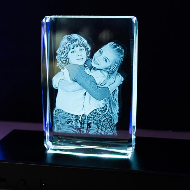 Cube en verre personnalisé gravé en 3D avec photo d’un couple enlacé, mis en valeur par un socle lumineux rotatif à LED verte pour un effet décoratif unique.