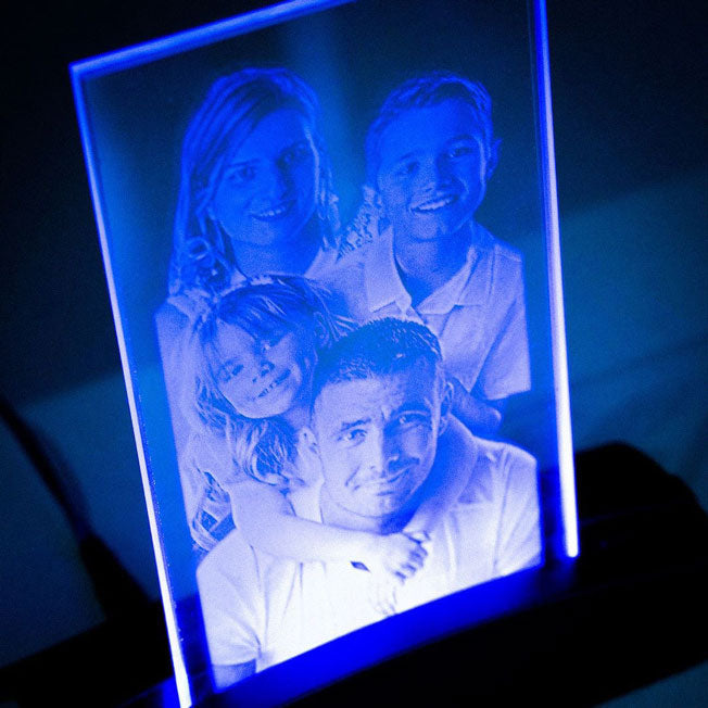 Plaque photo en verre gravée représentant une famille, posée sur un socle tunnel LED bleu qui illumine la gravure avec élégance et intensité.