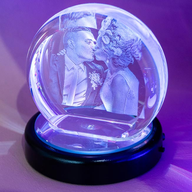 Un couple de mariés s’embrasse, gravé en 3D dans un bloc en forme de demi-lune en verre. Ce bloc lumineux rend le souvenir de mariage éternel.