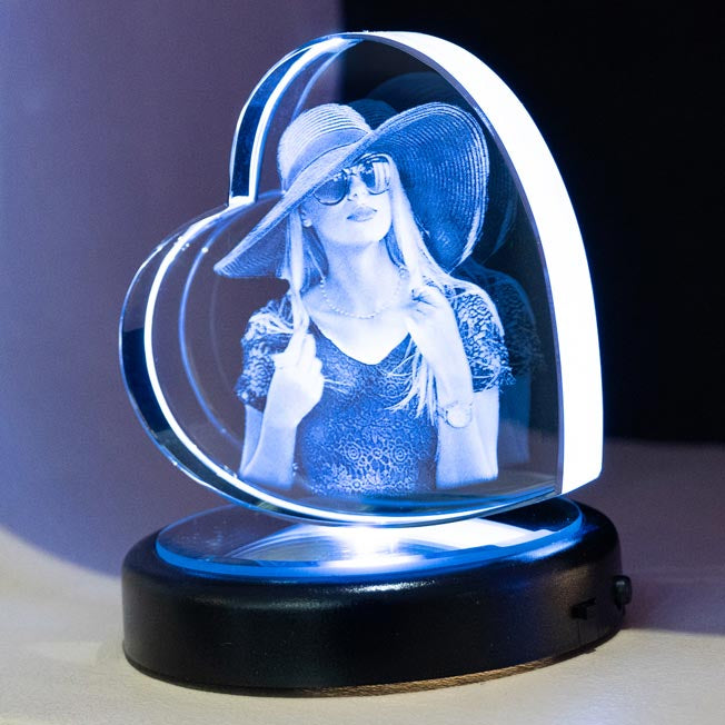 Une jeune femme avec un chapeau est gravée en 3D dans un bloc en forme de cœur en verre. Cadeau personnalisé original et raffiné avec socle lumineux.