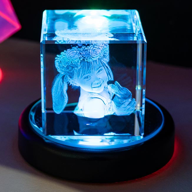 Une fillette avec une couronne de fleurs est gravée dans un cube de verre, éclairé par LED. Ce bloc photo en verre 3D est un souvenir d’enfance unique et lumineux.