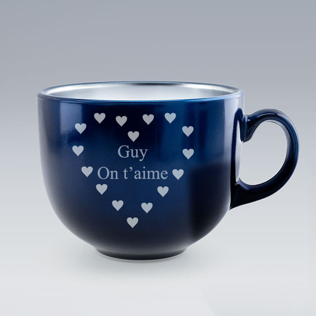 Tasse Jumbo bleue personnalisée avec le texte "Guy On t’aime", gravé au centre d’un cœur formé de petits cœurs, sur fond uni gris.
