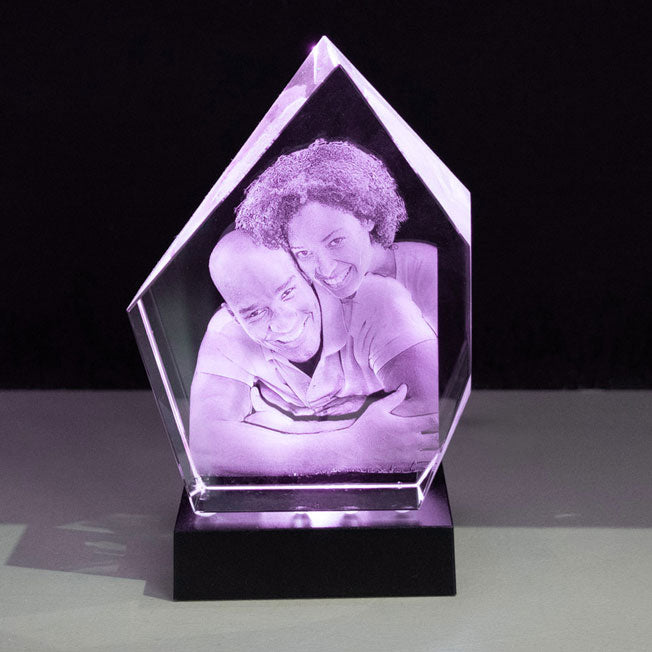 Trophée en verre Prestige 16 cm avec gravure 3D d’un couple enlacé, sublimé par une lumière violette de son socle lumineux. Cadeau personnalisé idéal.