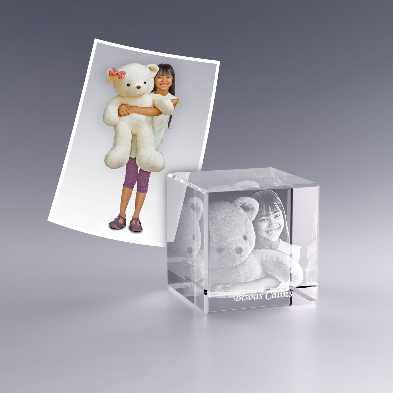 Gravure laser 3D dans un cube en verre de 4 cm représentant une enfant serrant un gros ours en peluche, avec l’inscription "Bisous Câlins".