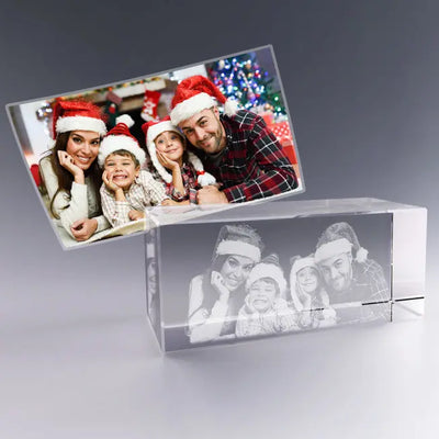 Bloc en verre rectangulaire gravé en 3D avec le portrait d’une famille portant des bonnets de Noël, reproduit à partir de la photo en couleur posée derrière.