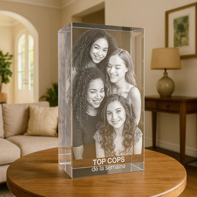 Bloc en verre vertical de 30 cm gravé en 3D avec cinq amies souriantes et l’inscription “TOP COP’S de la semaine”, posé sur une table dans un salon.