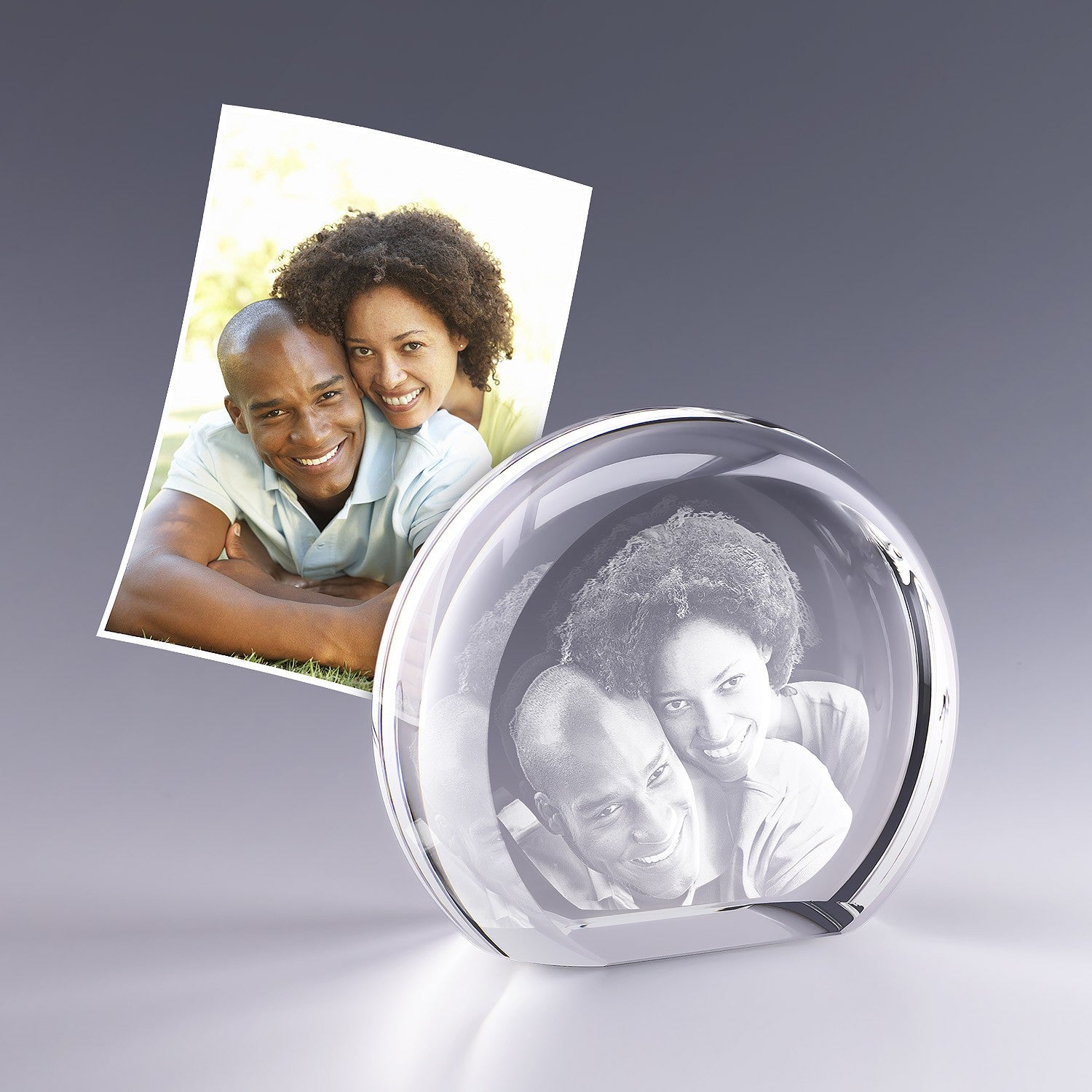 Bloc en verre rond en forme de demi-lune, gravé en 3D avec le portrait d’un couple enlacé, reproduit à partir de la photo posée à côté.