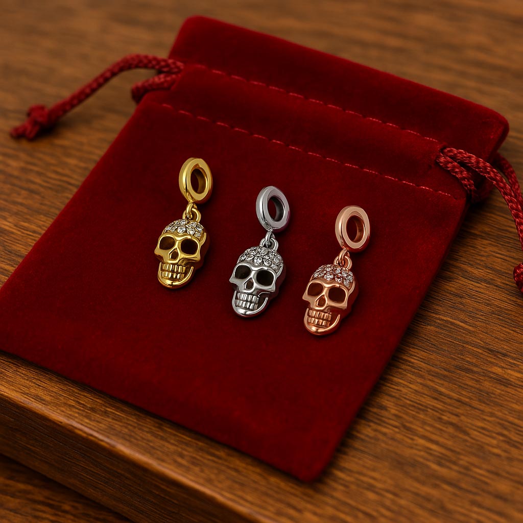 Ensemble de trois charms tête de mort en finitions dorée, argentée et rose doré, posés sur une pochette en velours rouge.
