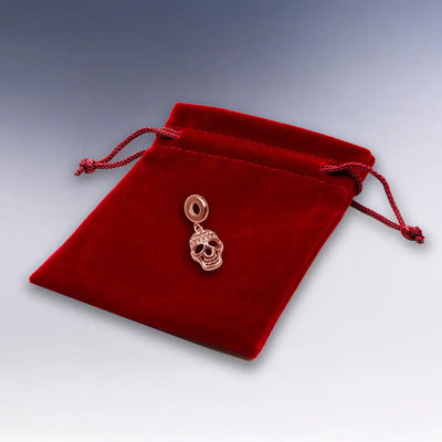 Charm tête de mort finition rose doré avec cristaux scintillants, présenté sur une élégante pochette en suédine rouge.