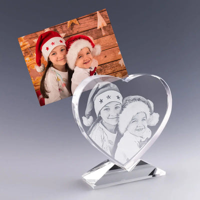 Cœur en Verre Gravé 2D avec photo et texte personnalisés – Cadeau de Noël – Deux enfants souriants portent des bonnets rouges devant un décor en bois festif. Leur image est gravée avec finesse dans un cœur en verre sur socle, un cadeau personnalisé plein de tendresse pour célébrer la magie de Noël.
