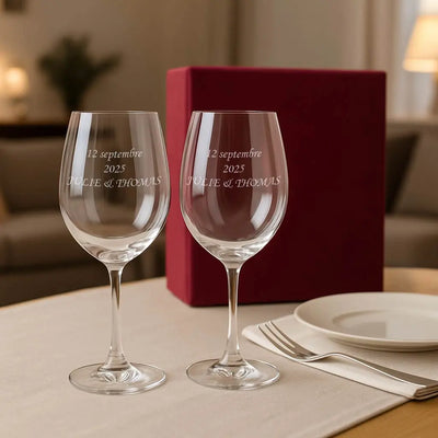 Coffret cadeau contenant deux verres à vin personnalisés par gravure laser avec les prénoms Julie & Thomas et la date 12 septembre 2025, posés sur une table dressée dans une ambiance chaleureuse.