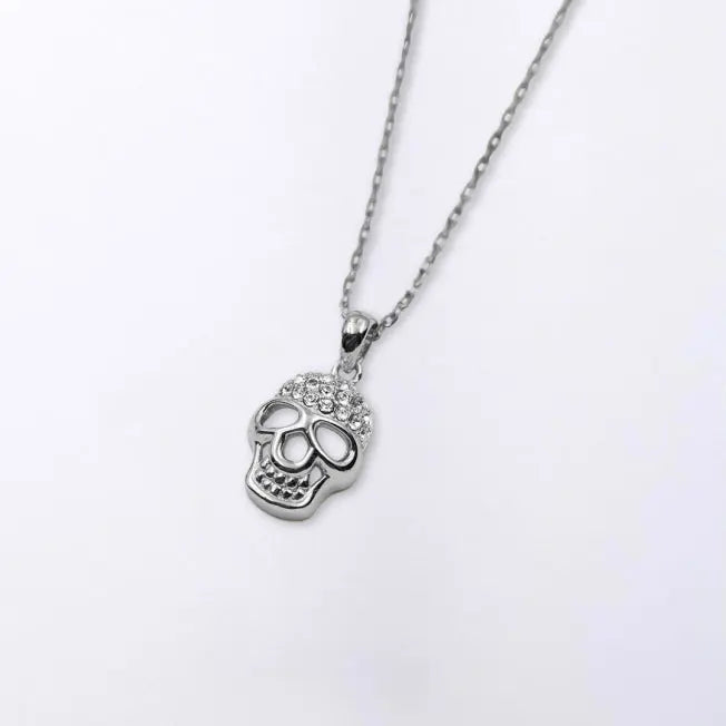 Collier Tête de Mort argenté avec chaîne assortie, posé sur fond clair, détails scintillants sur le crâne.