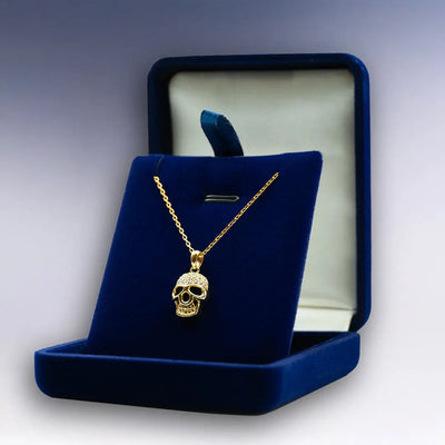 Collier Tête de Mort doré dans boîte bleu velours ouverte, design éclatant et esprit rebelle assumé.
