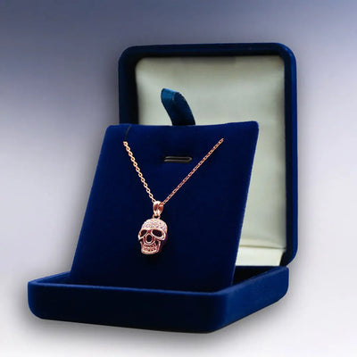 Collier Tête de Mort rose doré exposé dans un écrin velours bleu ouvert, parfait pour un cadeau rock chic.