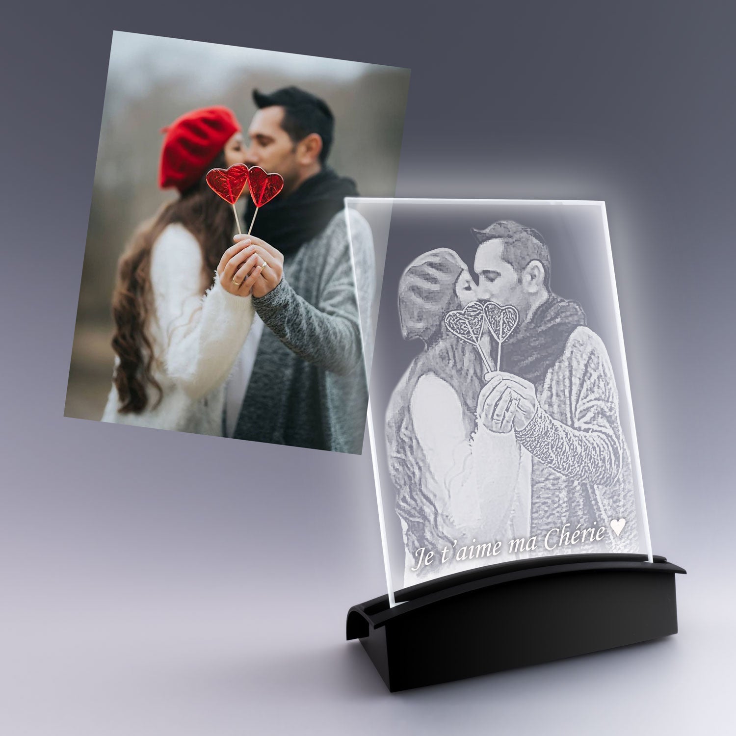 Grande plaque photo verticale en verre avec gravure 2D personnalisée d’un couple amoureux tenant des cœurs, posée sur un socle lumineux noir.