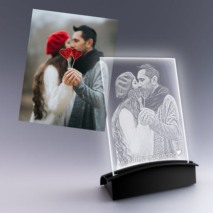 Grande plaque photo verticale en verre avec gravure 2D personnalisée d’un couple amoureux tenant des cœurs, posée sur un socle lumineux noir.
