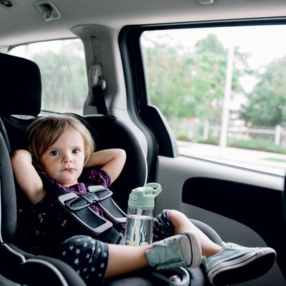Enfant assis dans un siège auto tenant une bouteille pour enfant en Tritan personnalisée, idéale pour les sorties et les voyages.