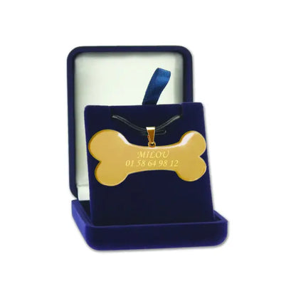Pendentif en forme d’os doré personnalisable avec nom et numéro de téléphone, présenté dans un écrin en velours bleu.
